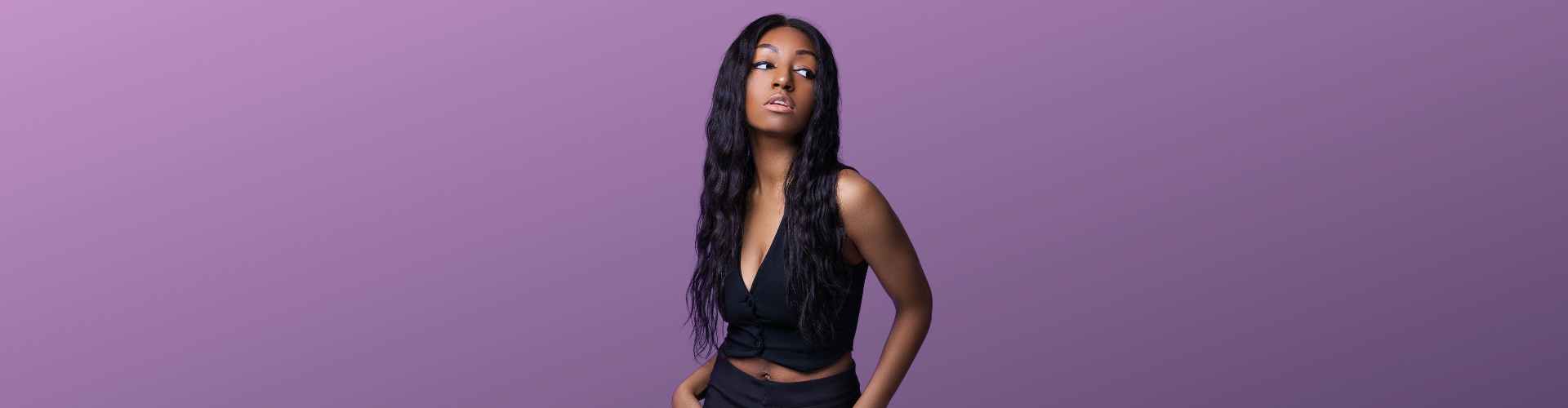 Yasmine Benoit in a black top and trousers against a purple background