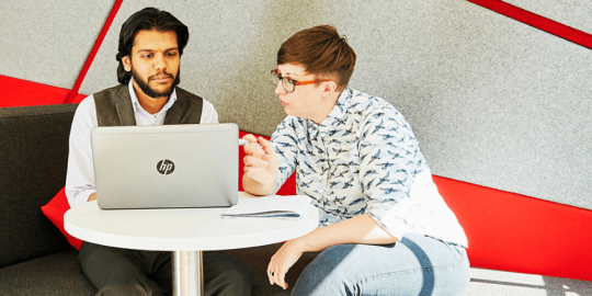 Two employees at desk looking at laptop