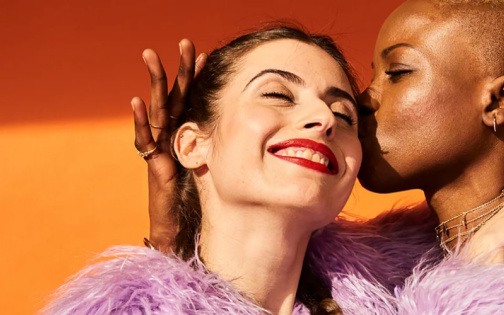 Two people, one a Black person, one white, embracing in front of an orange background