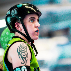 White person side-on in green roller derby outfit against a blue background 